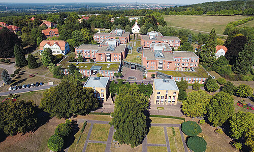 Luftaufnahme des Standortes Wiesloch. Es sind verschiedene Gebäude zu sehen. Die Anlage ist umrandet von zahlreichen Bäumen und Grünflächen und Feldern.