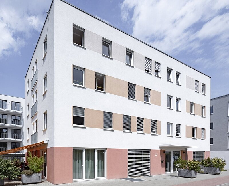 Moderner vierstöckiger Gebäudekomplex bei blauem Himmel.