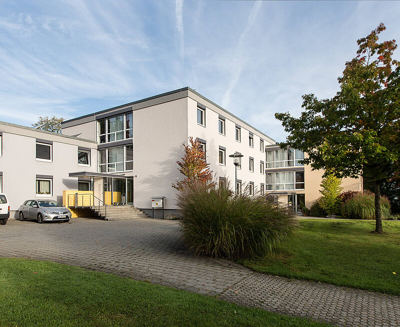 Ansicht auf einen Weg welcher durch eine Grünanlage zum dreistöckigen Verwaltungsgebäude führt.