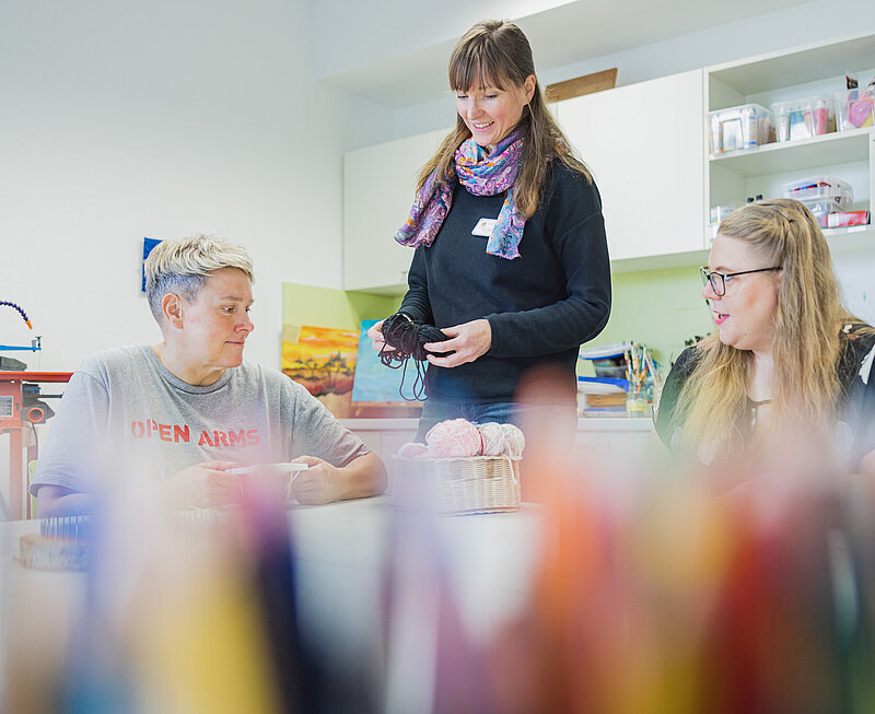 Ergotherapie-Wiesloch.jpg Drei Frauen befinden sich in einem Raum. Auf dem liegt ein Korb mit Wolle und ein Brett zum Knüpfen.