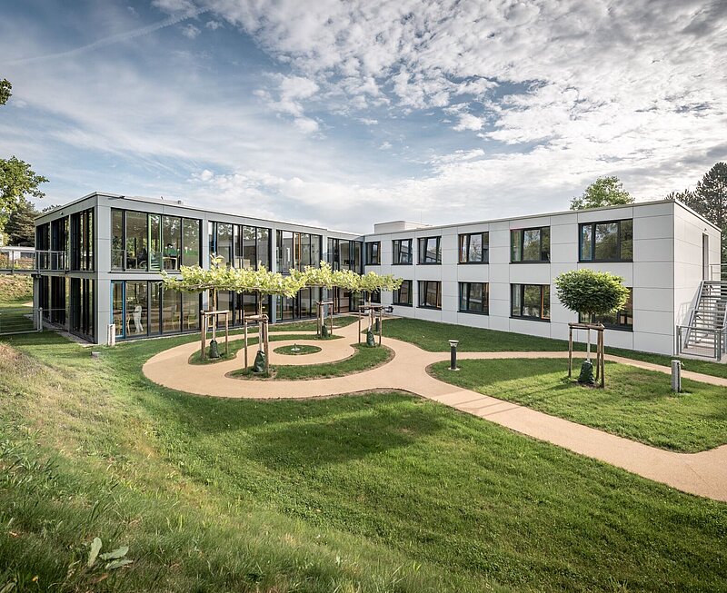 Modernes zweistöckiges Klinikgebäude mit vielen großen Fenstern inmitten einer Grünanlage. Im Gebäude befindet sich die Alterspsychiatrie.