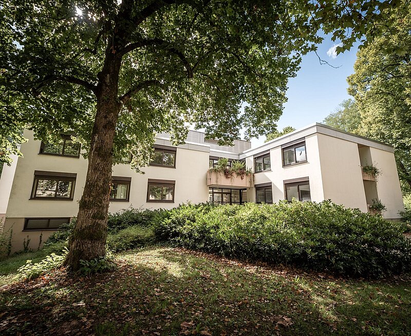 Modernes dreistöckige Klinikgebäude umsäumt von Bäumen und Bepflanzung.