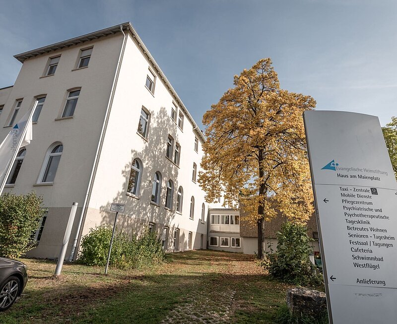 Ansicht auf die vierstöckige psychotherapeutische Tagesklinik umrandet von Bäumen.