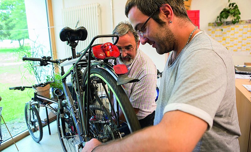 Zwei Männer reparieren gemeinsam ein Herrenfahrrad.