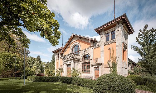 Historische Festhalle inmitten einer grün bewachsenen Parkanlage.